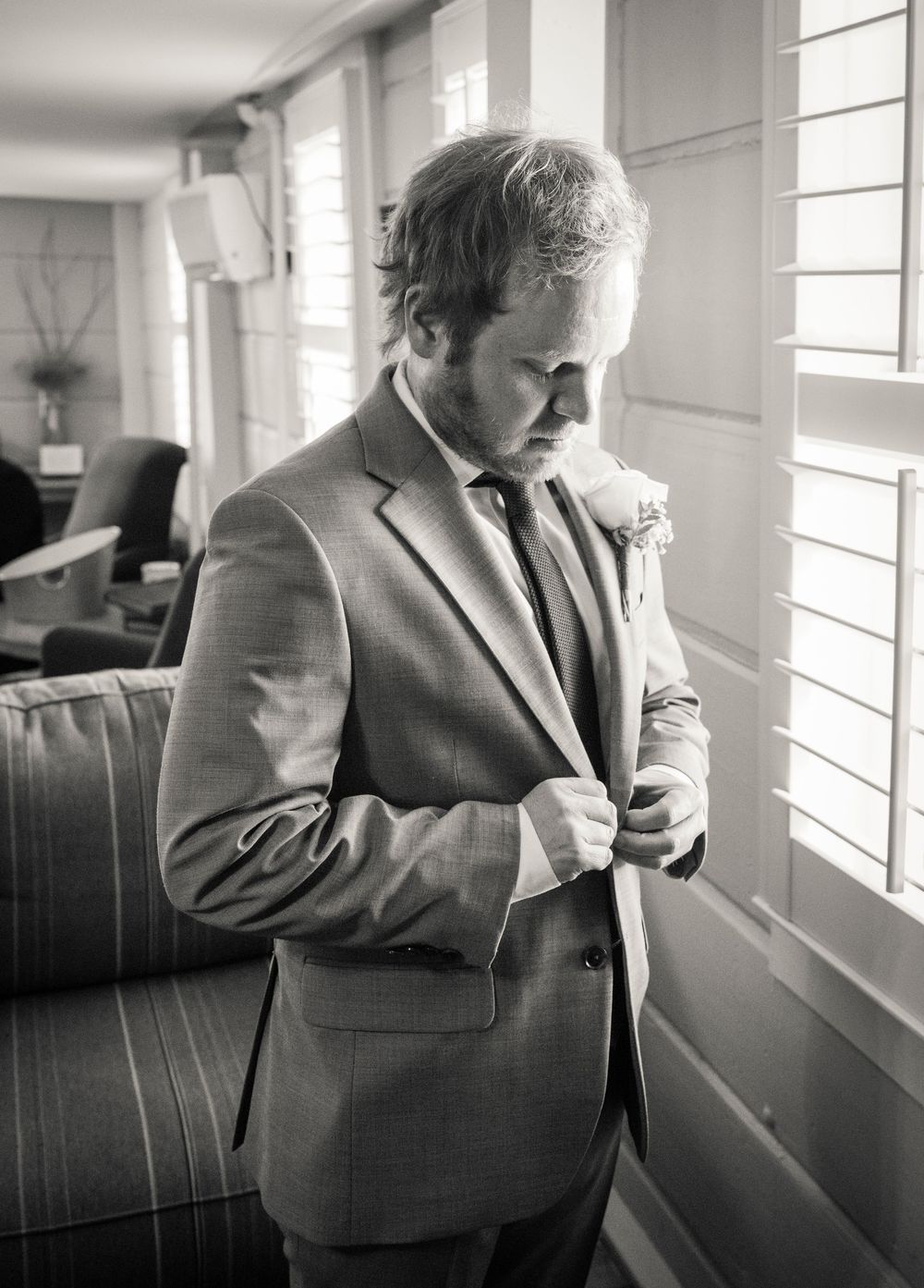 Black and white sequence showing a person in a suit adjusting their tie near windows in an interior space.