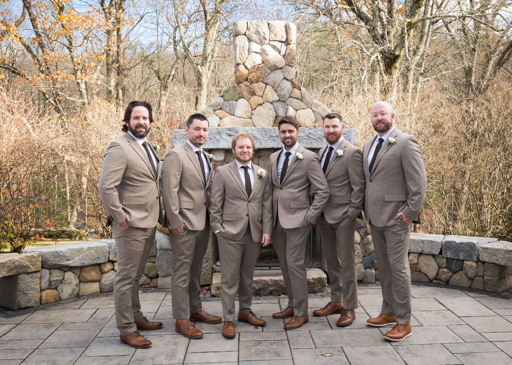 Groomsmen in matching gray suits pose together on stone steps outdoors.