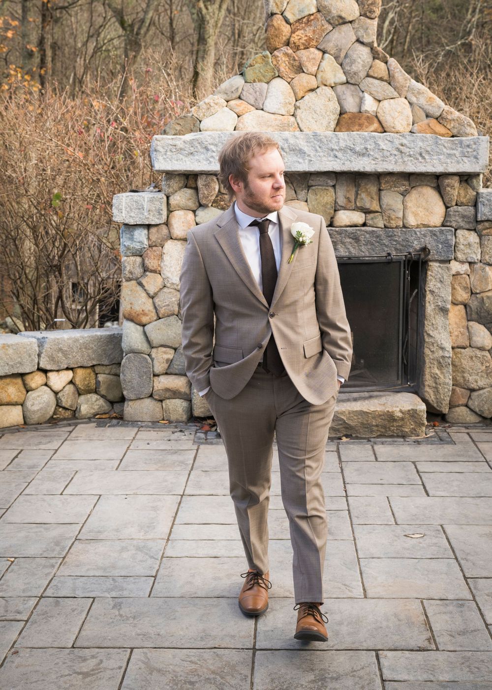 Person in gray suit walking along stone patio with rustic stone wall backdrop.