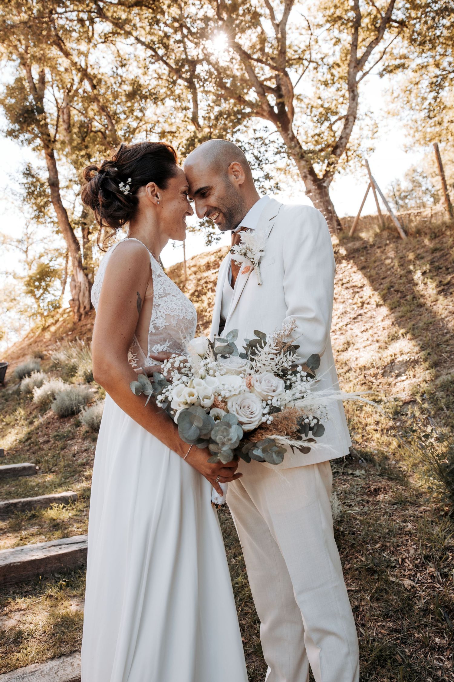 Newlyweds share tender moment in white attire against natural outdoor setting. Domaine la Plume photographe mariage