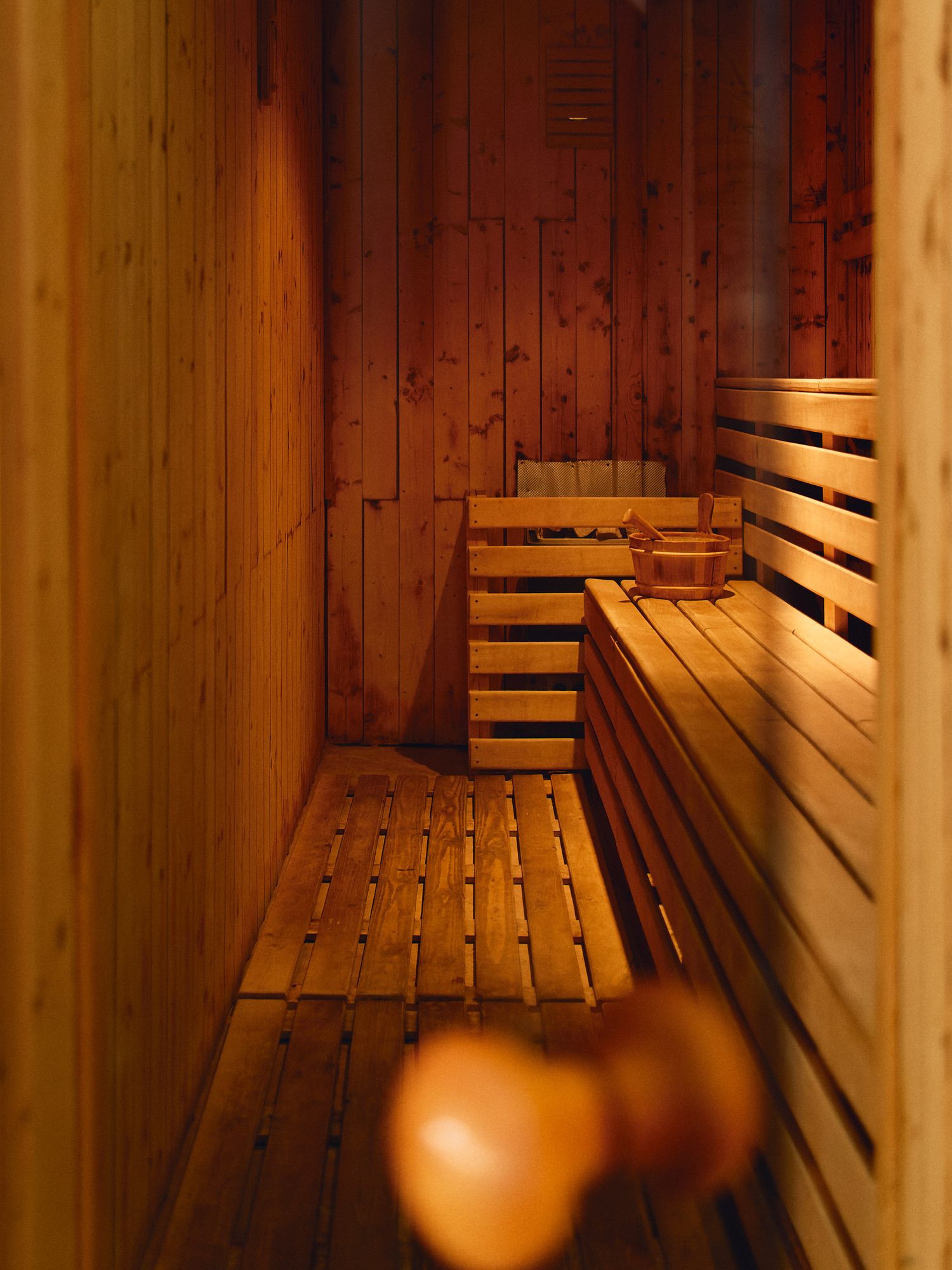 Interior view of a wooden sauna with empty tiered benches illuminated by warm lighting.