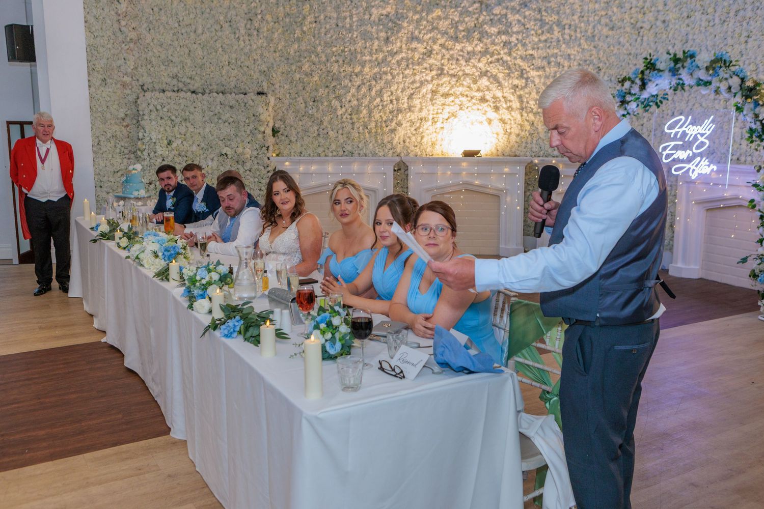 Guests at a wedding reception dance and celebrate together on a wooden dance floor near decorated tables.