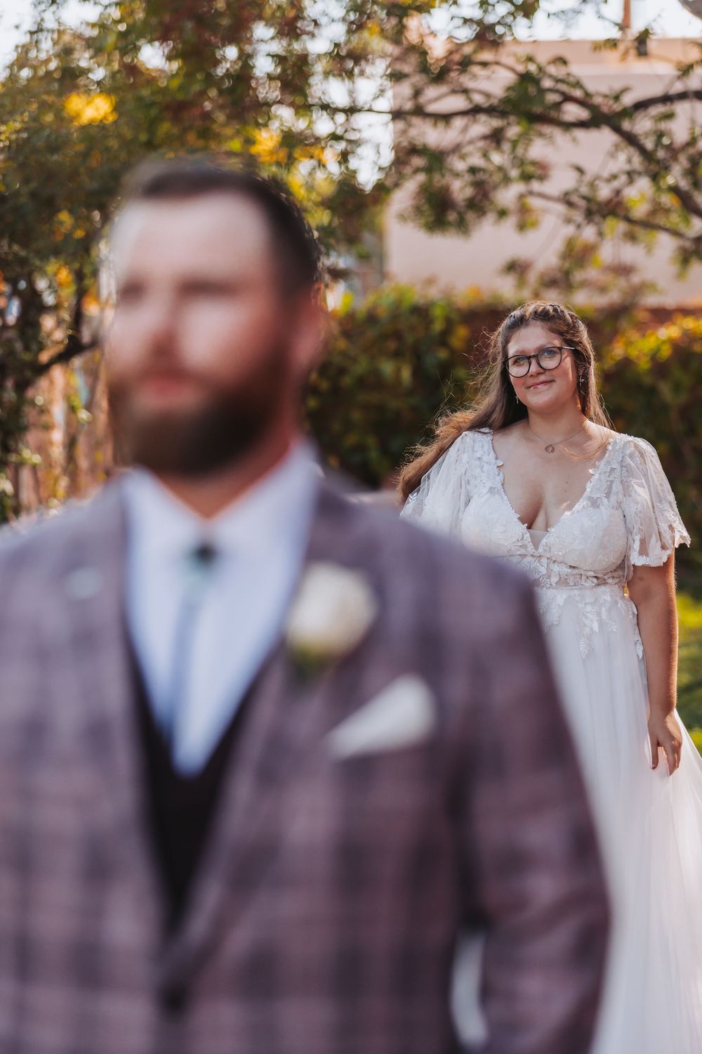 A wedding couple poses outdoors during golden hour with soft bokeh lighting and autumn trees in the background.