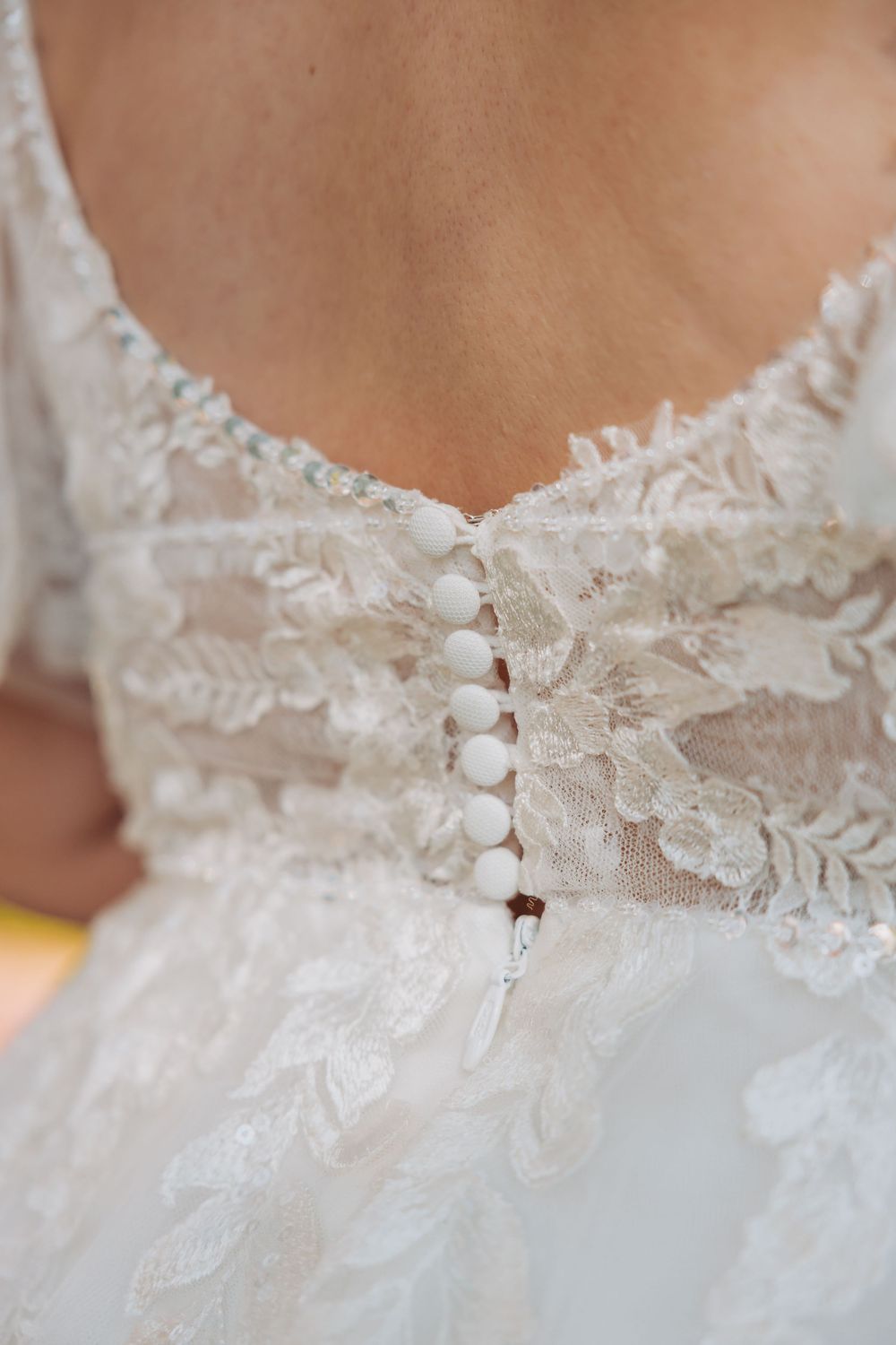 Close-up detail of delicate white lace trim and floral appliques on a wedding dress neckline.