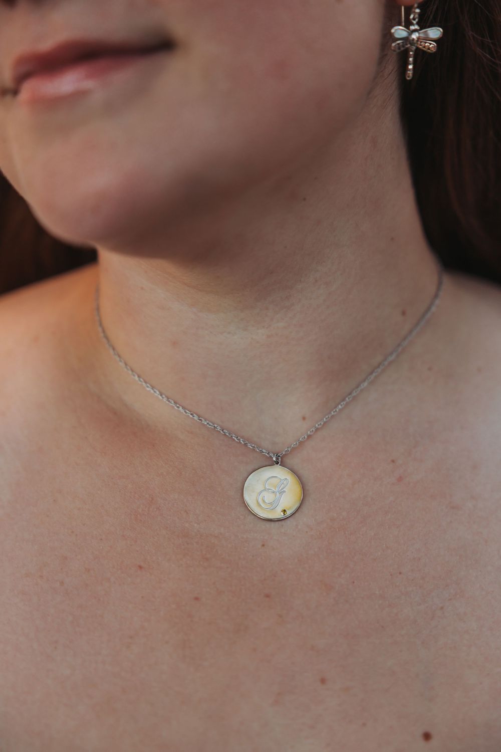 A close-up view of a silver necklace with a circular pendant worn around a neck.