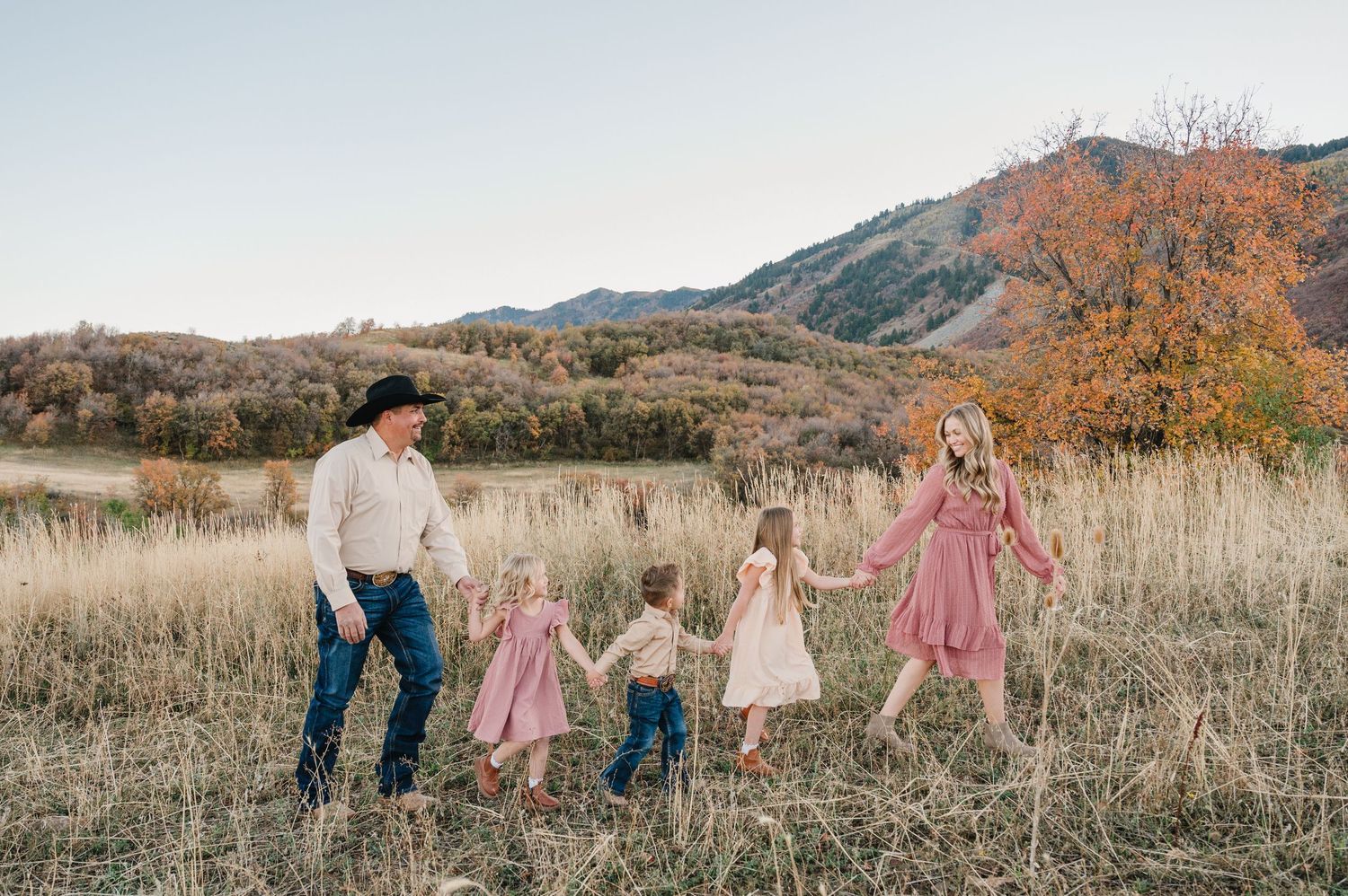A family walks together through a golden autumn field with mountains in the background during sunset.