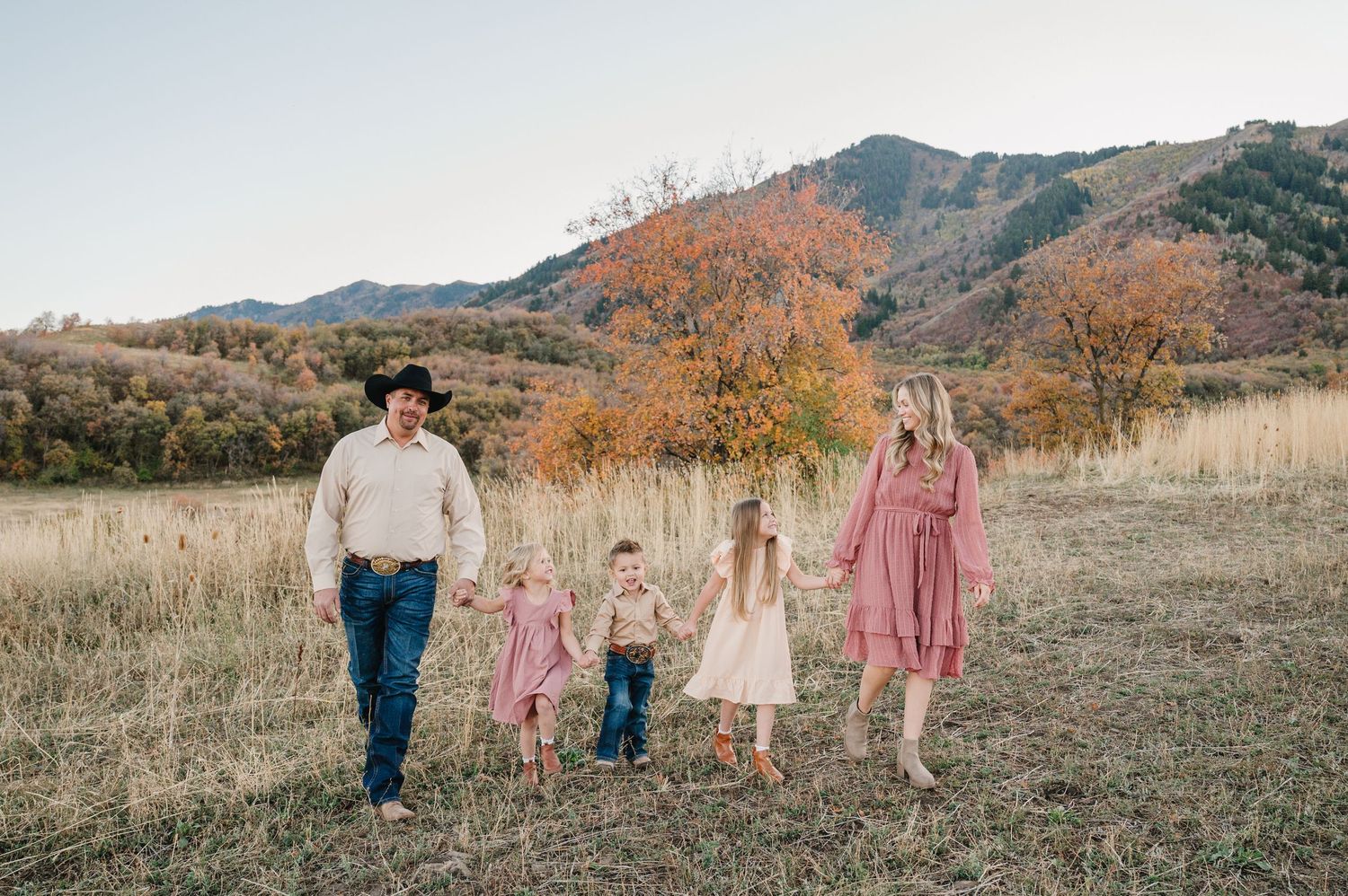 A group walks together through a golden autumn field with mountains in the background during sunset.