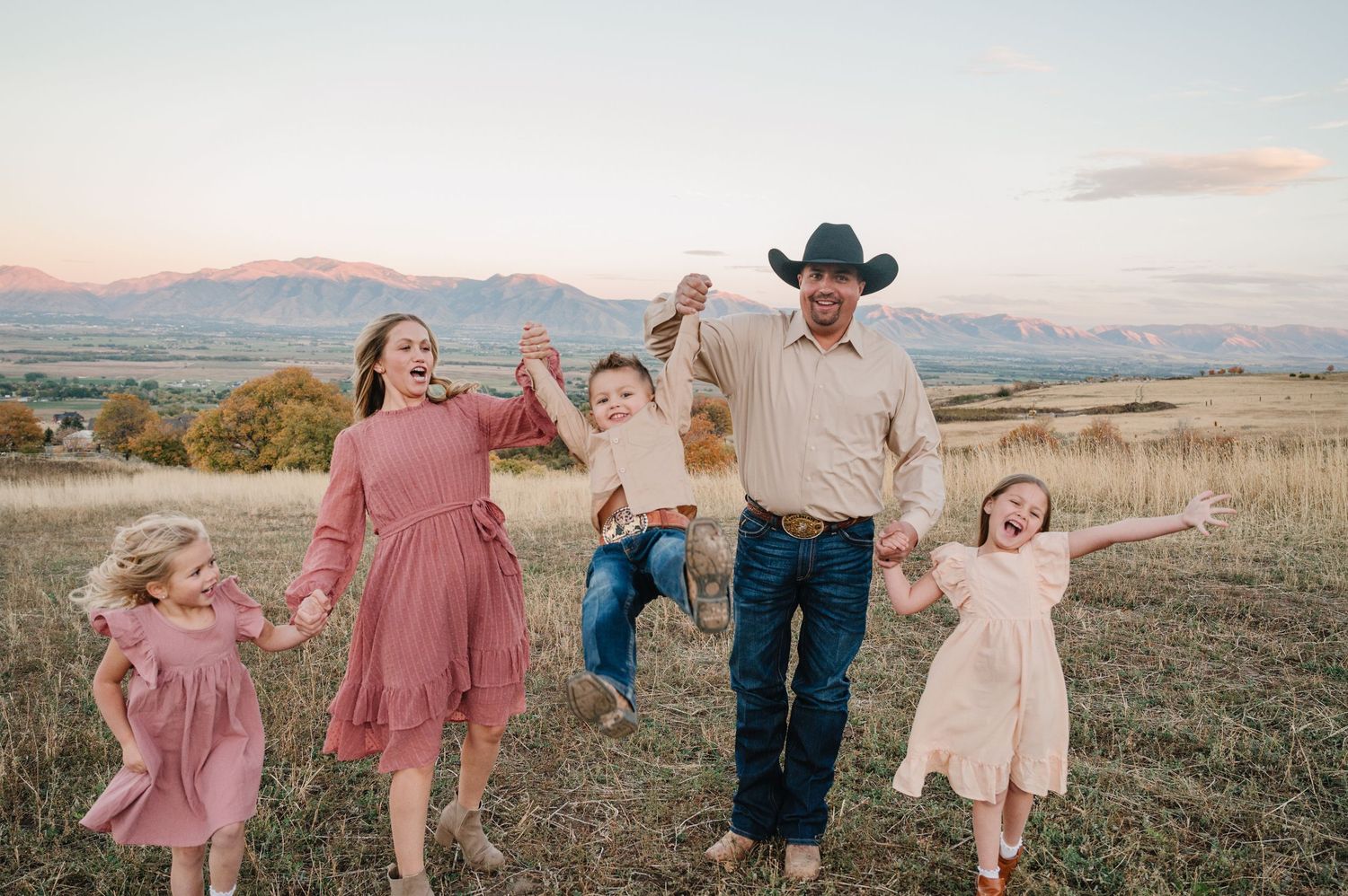Family enjoying a sunset photoshoot in a rustic field with mountains in the background.