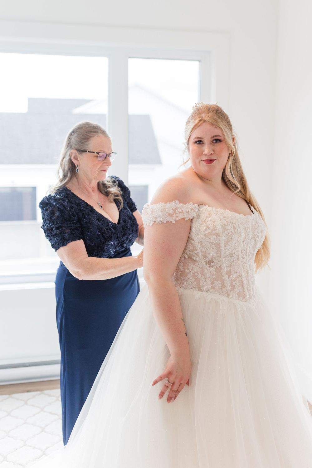 Wedding preparation scene showing a white lace wedding dress and navy blue dress in a bright room.