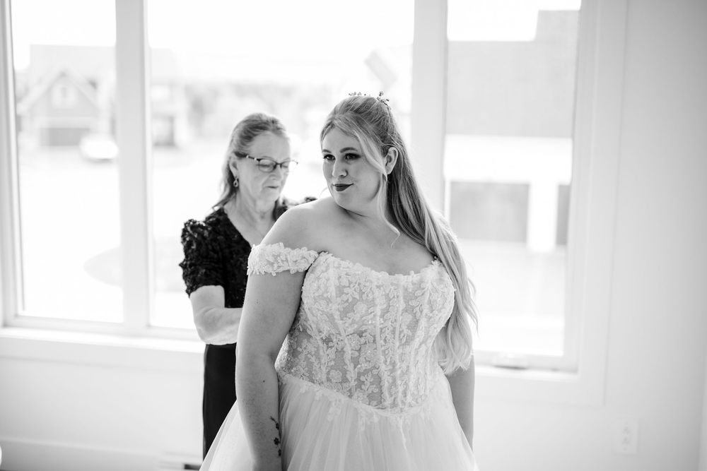 A black and white photograph showing a tender moment during wedding preparations in a bright interior space.