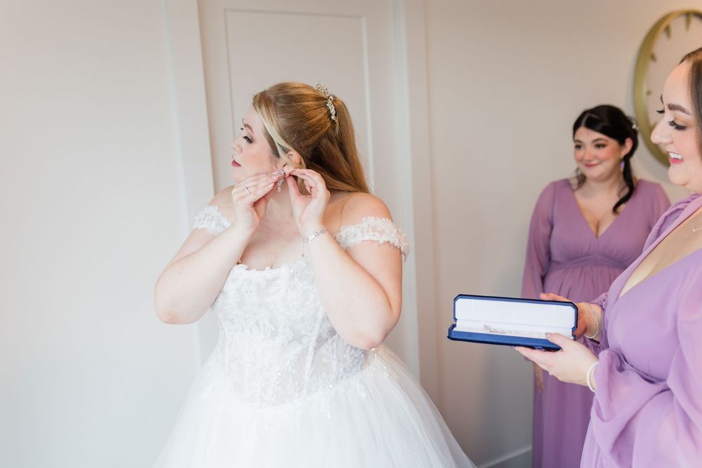 A bride and bridesmaids in purple dresses prepare for a wedding day in a sunlit room.