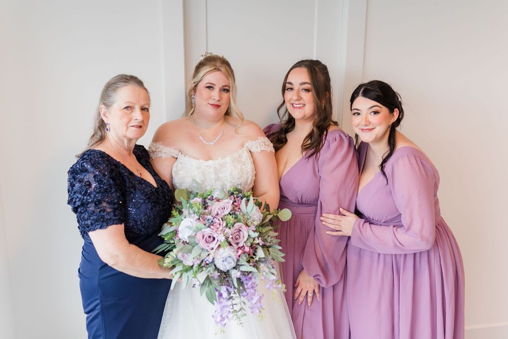 Wedding party wearing purple and navy dresses gathered together with bridal bouquet.