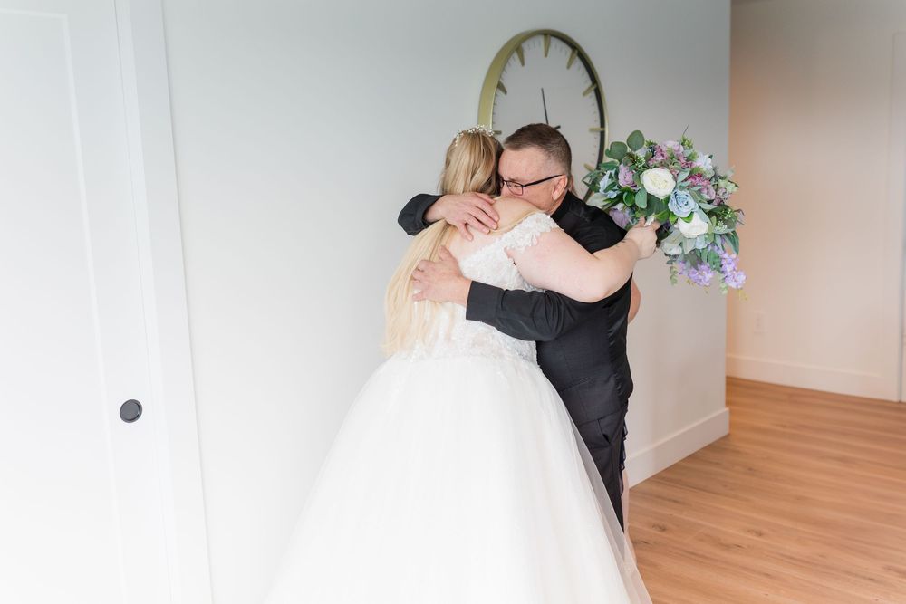 A romantic wedding couple dances together in an elegant room with wooden floors and white walls.