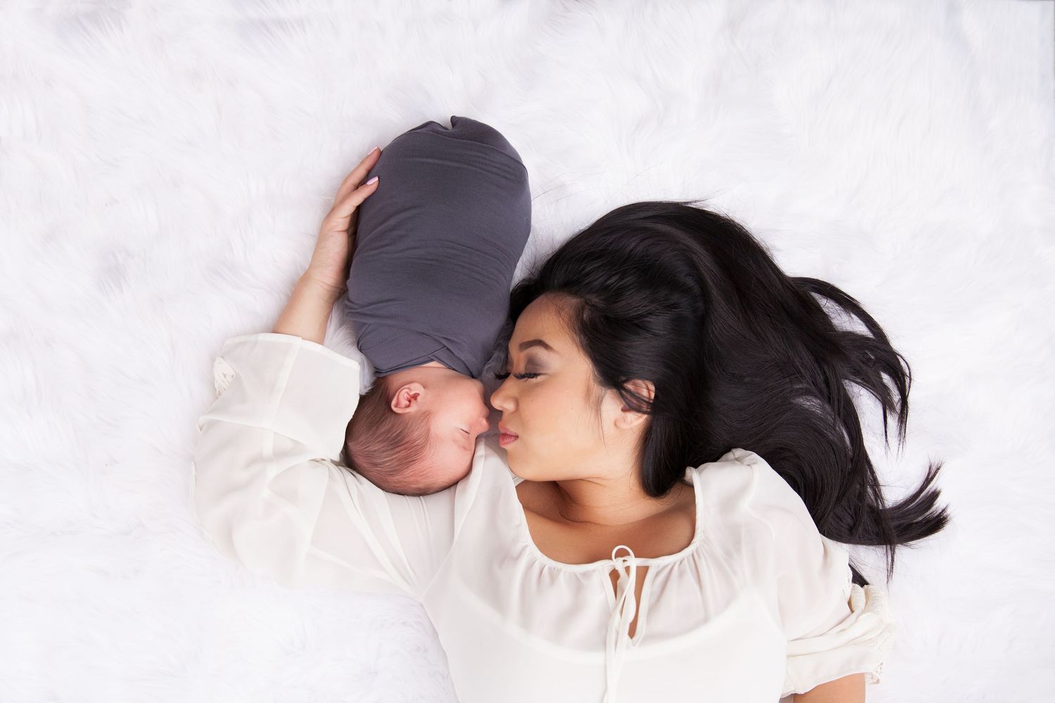 A couple lying down on white bedding share an intimate kiss with long dark hair flowing.