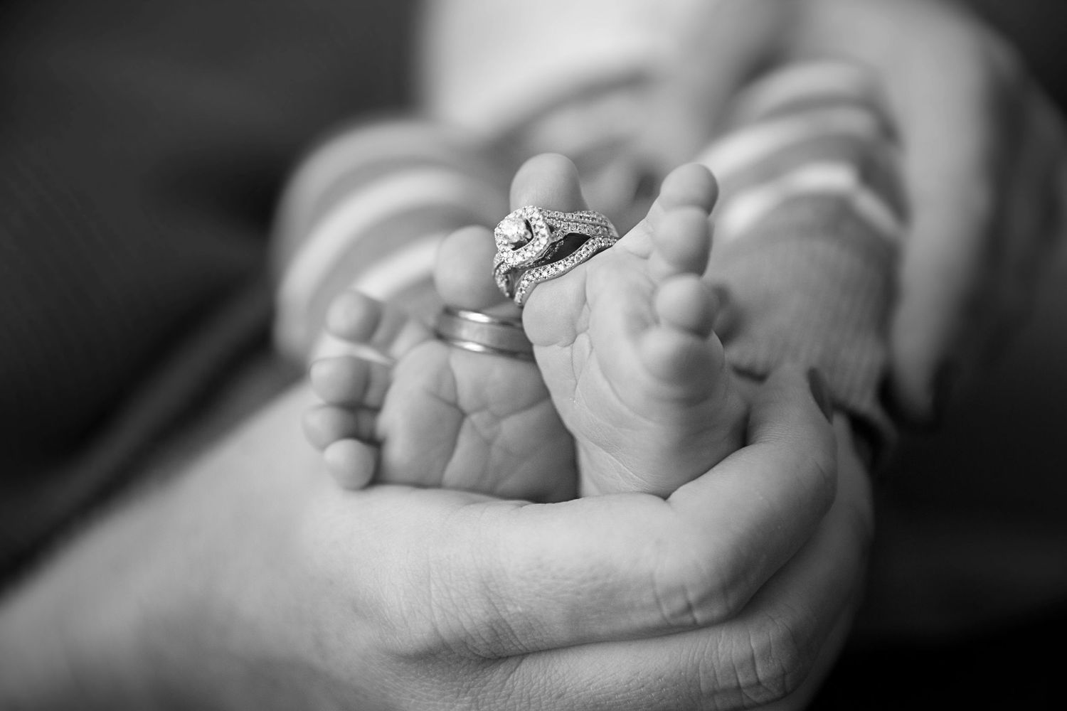 Black and white close-up of tiny newborn baby feet being gently held in adult hands.