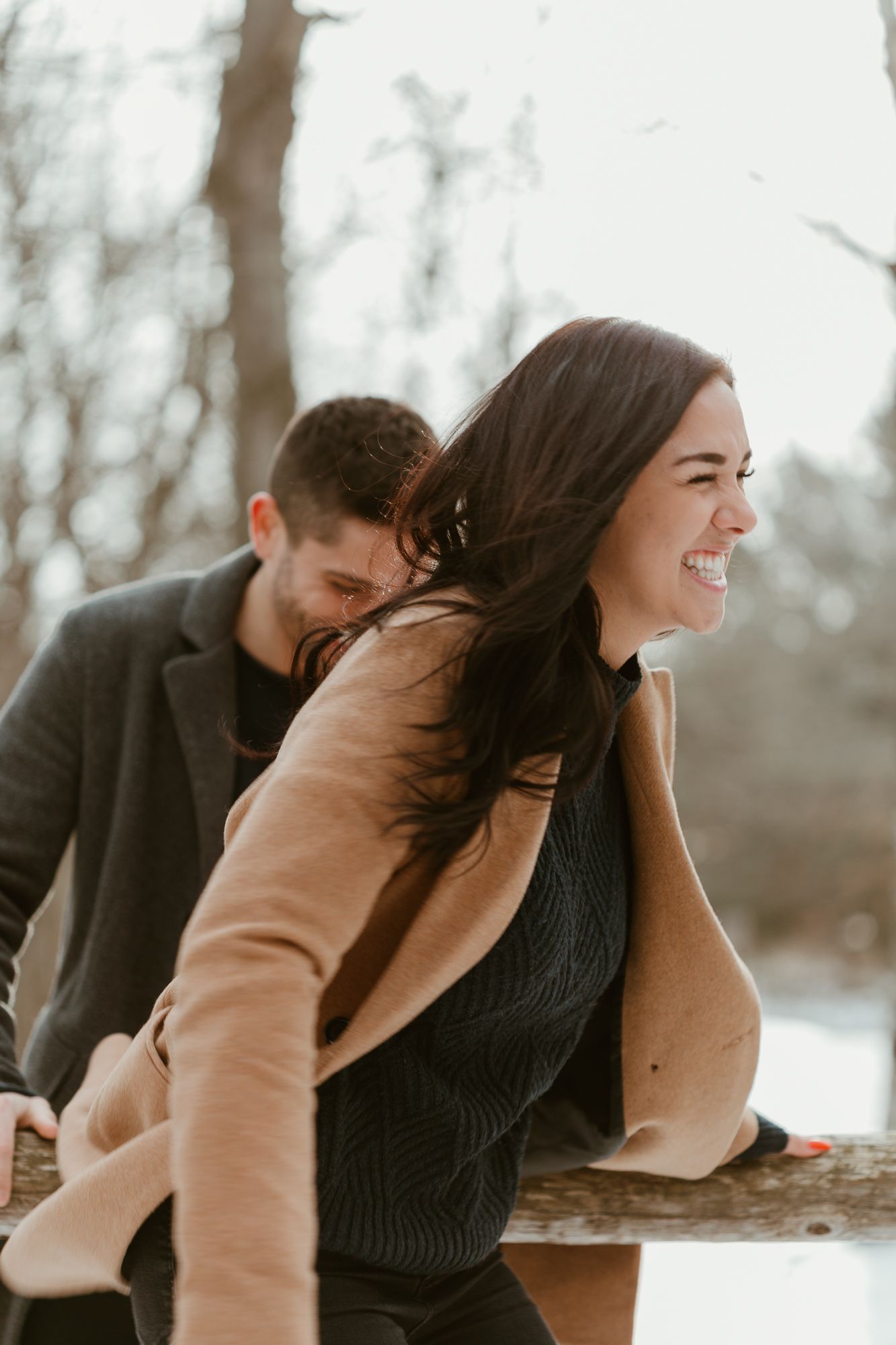 A couple shares joyful laughter together during a winter photoshoot in a snowy outdoor setting.
