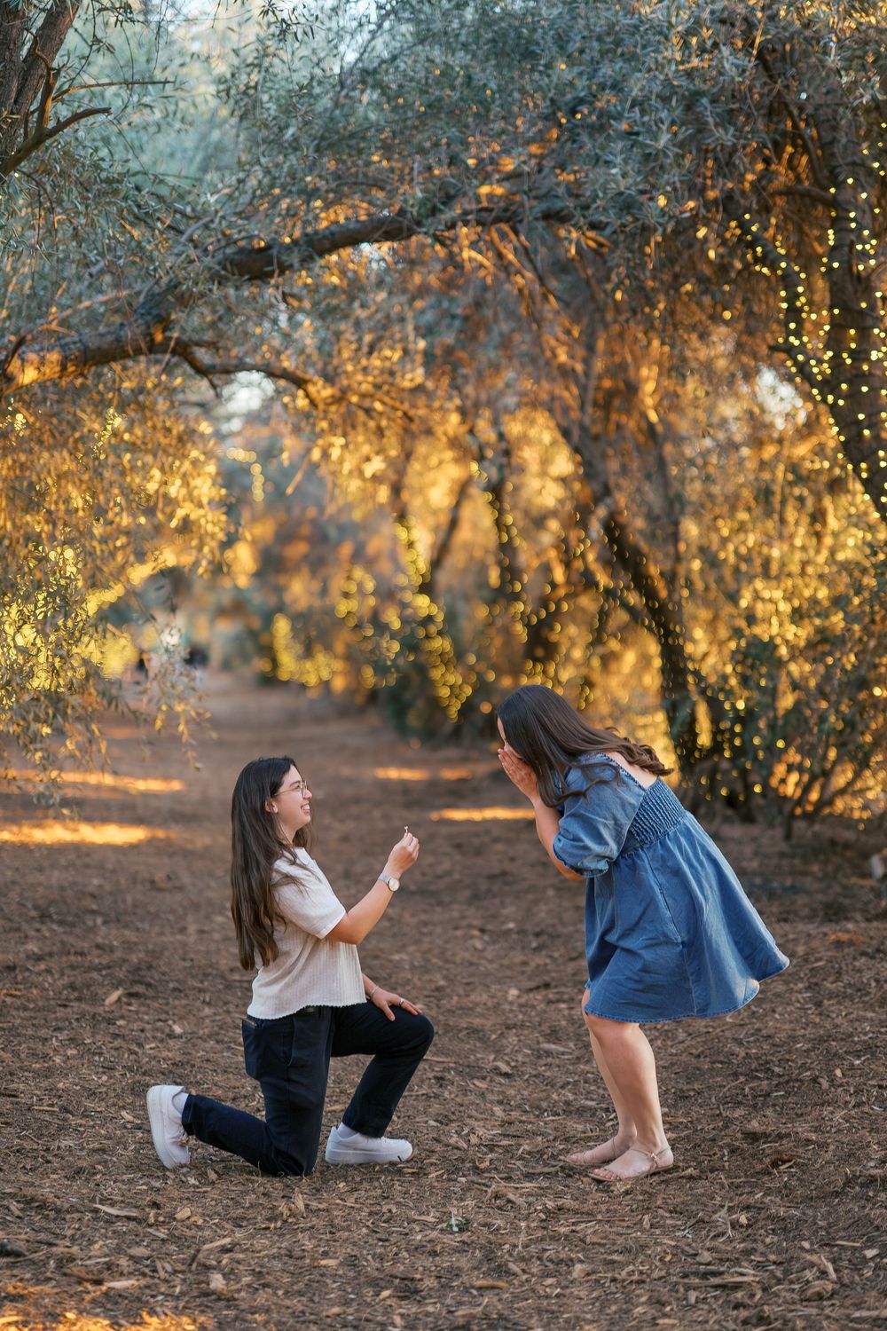 A romantic proposal scene on a dirt path surrounded by glowing autumn trees at golden hour.
