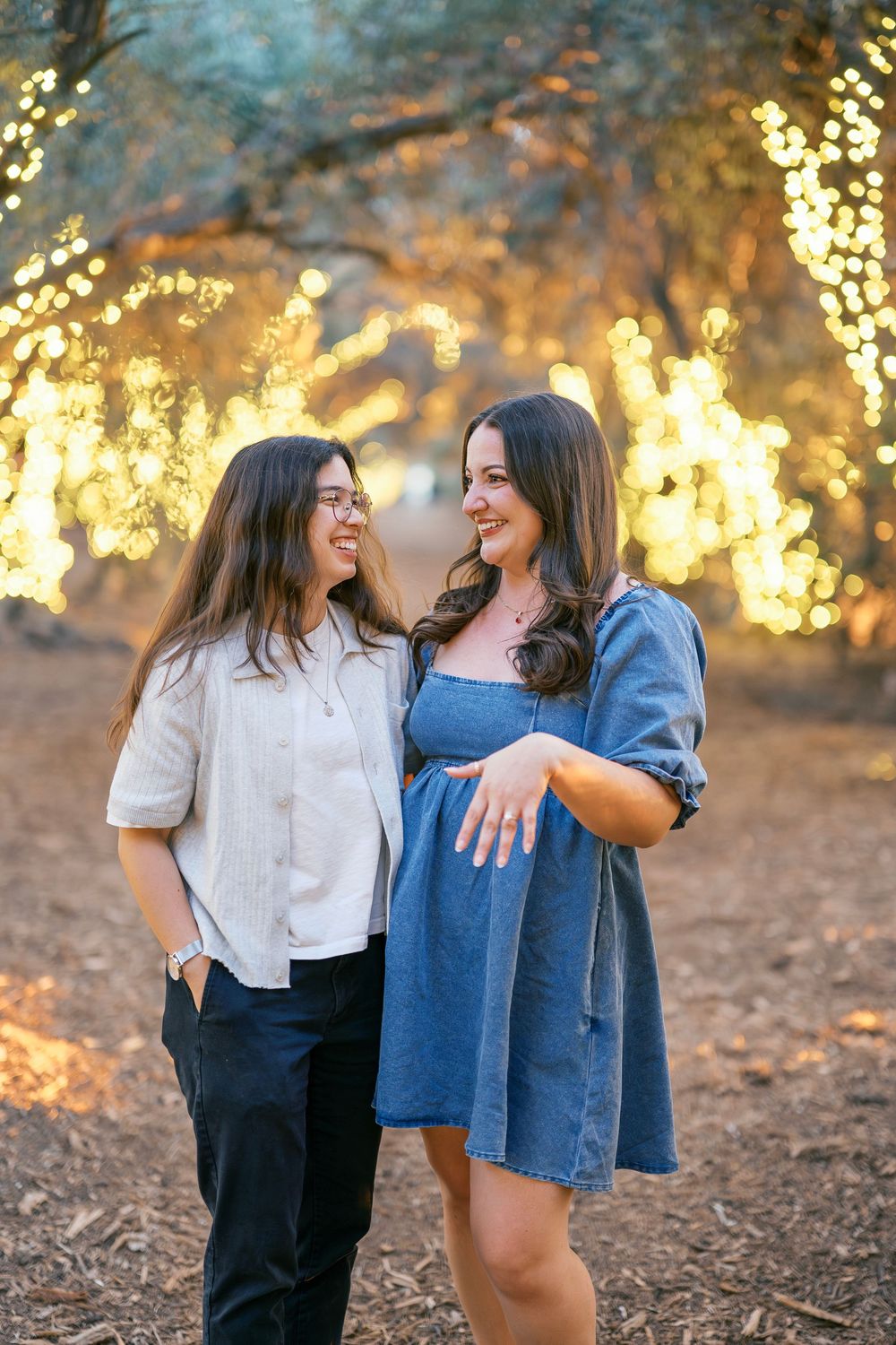 Two people sharing joyful laughter together under glowing string lights in a rustic outdoor setting.