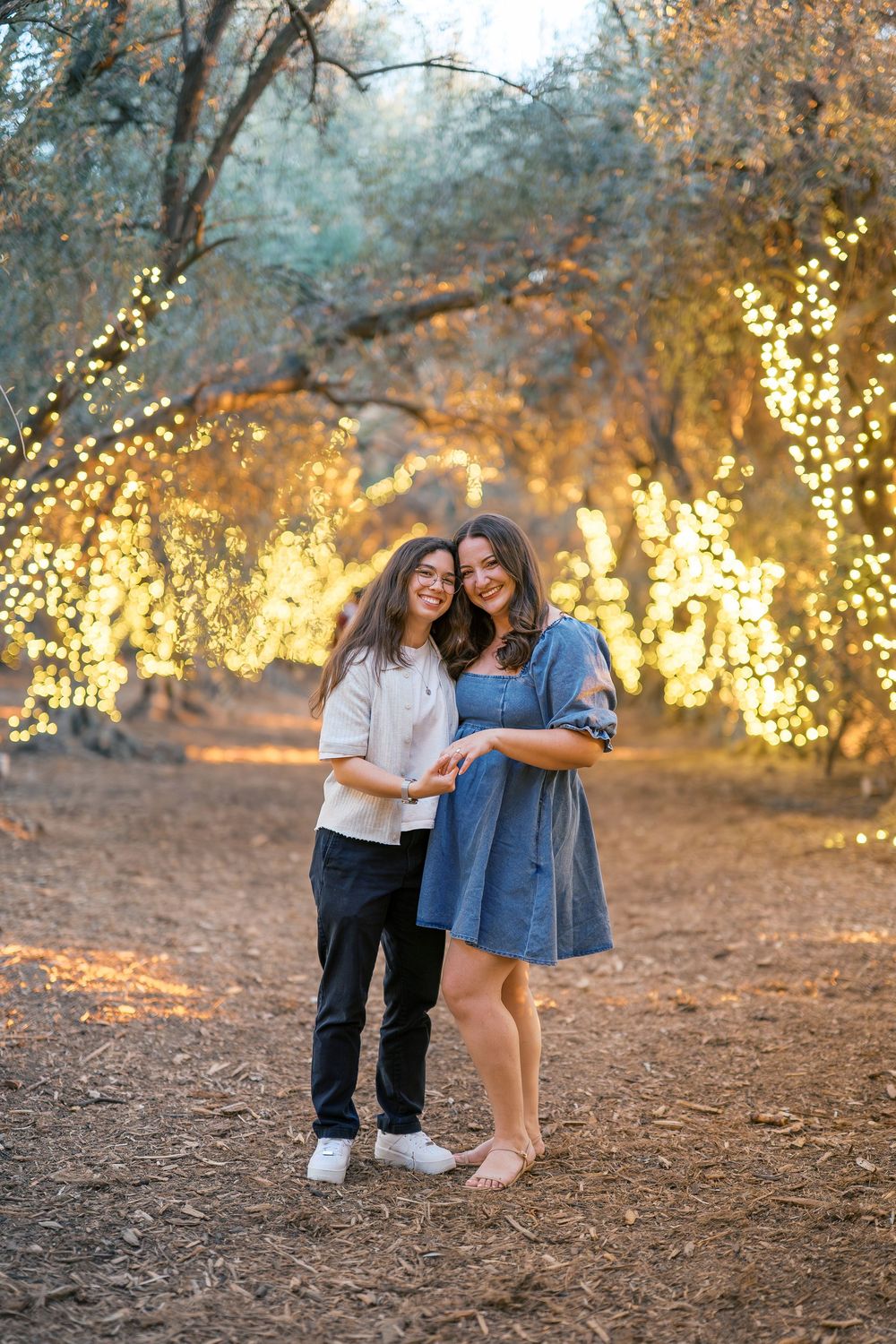 Friends celebrate joyfully together on a dirt path with magical fairy lights glowing in the trees.