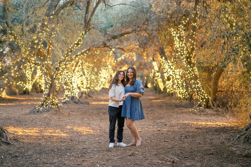 A group poses for autumn family photos in a sun-drenched wooded area with golden light filtering through trees.