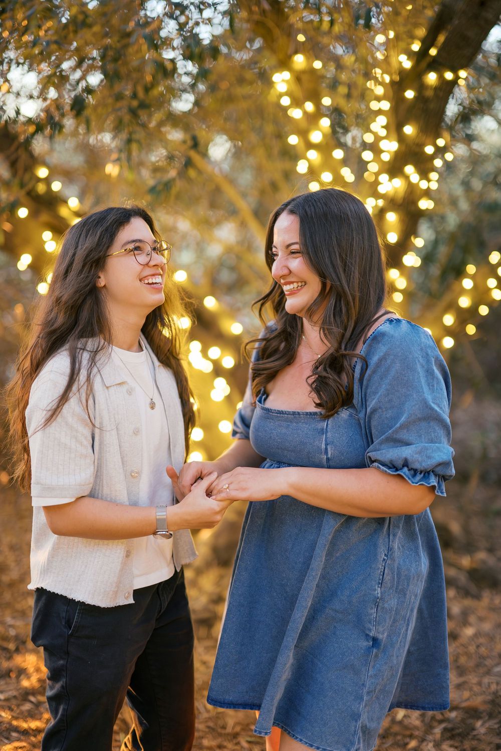 Two friends share joyful moments together under twinkling lights and autumn trees.