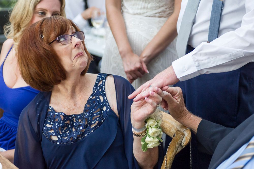 Elderly woman examines wedding ring while seated at an outdoor wedding ceremony celebration.