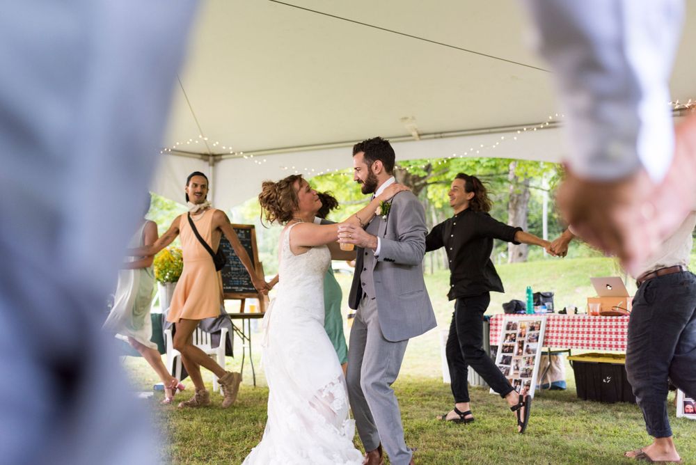Bride and groom share joyful first dance under white tent at outdoor summer wedding celebration.