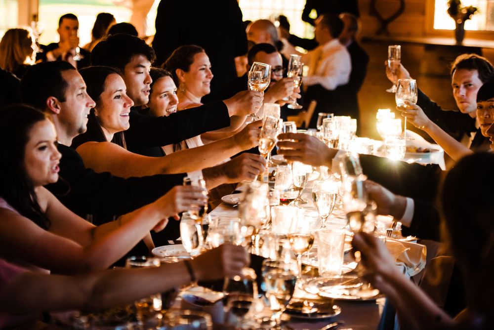 Wedding guests raise champagne glasses in a joyful toast at a candlelit reception dinner table.