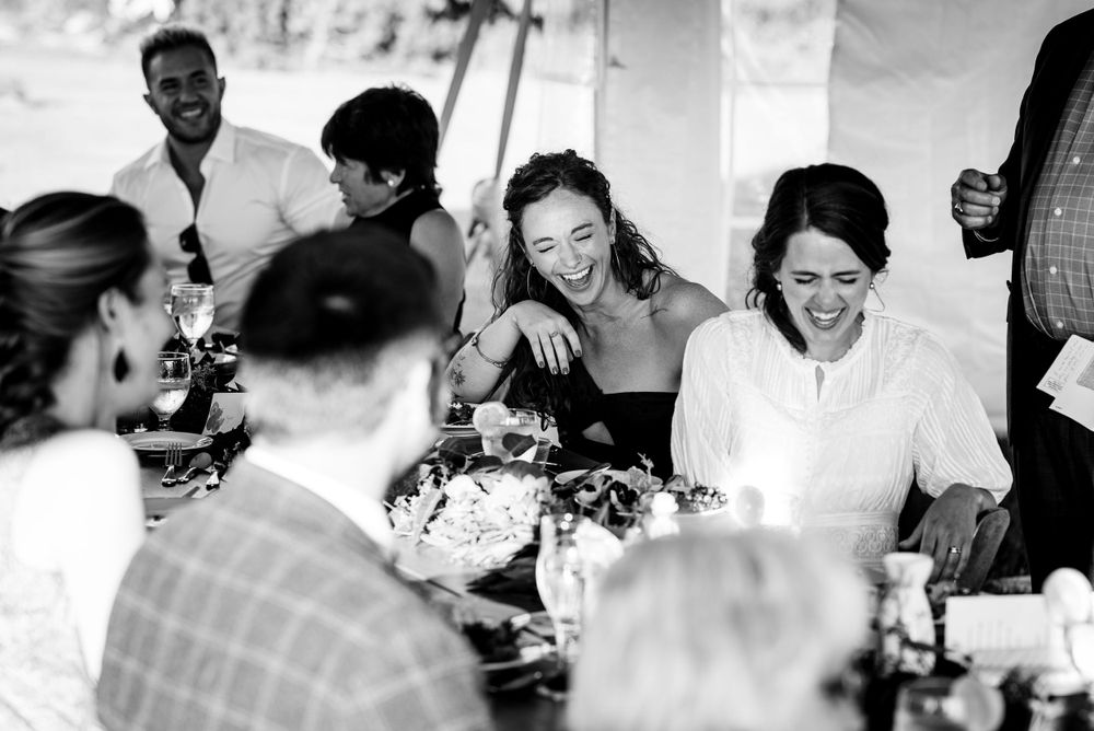 Guests laughing and socializing at wedding reception table in black and white photo.