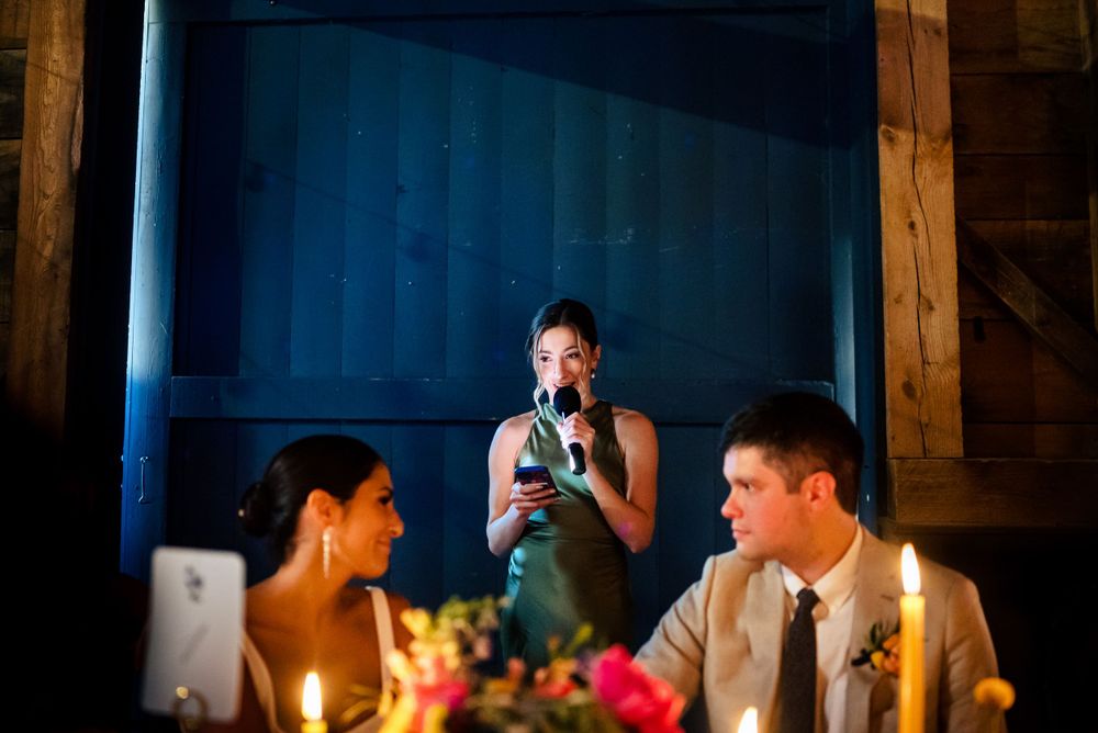 Wedding guest delivers heartfelt candlelit toast speech while bride and groom listen at the head table.