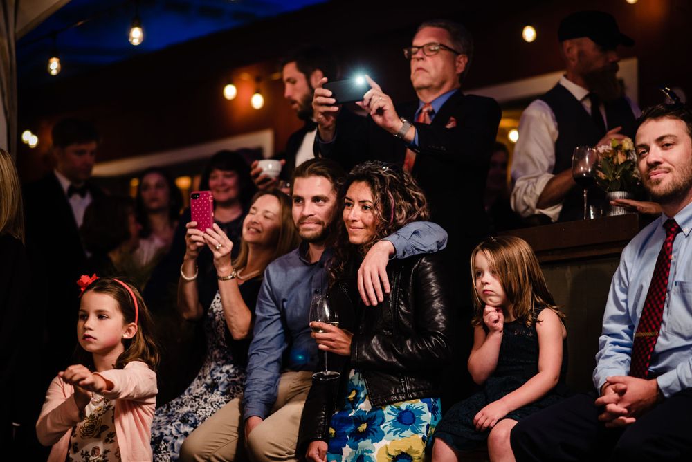 Wedding guests smiling and taking photos together at a lively indoor reception.