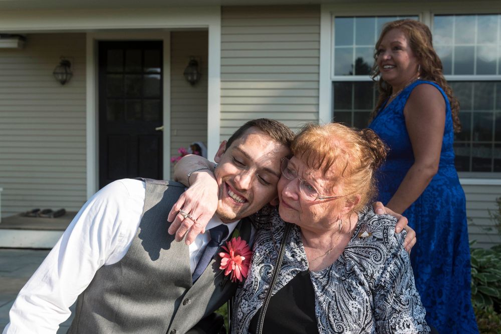 Young man in wedding attire hugging an elderly woman affectionately outdoors.