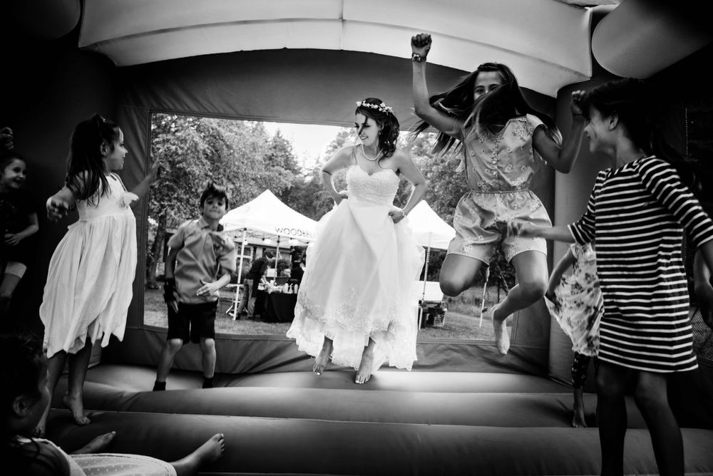 Bride jumping joyfully on a bouncy castle with guests at an outdoor wedding.