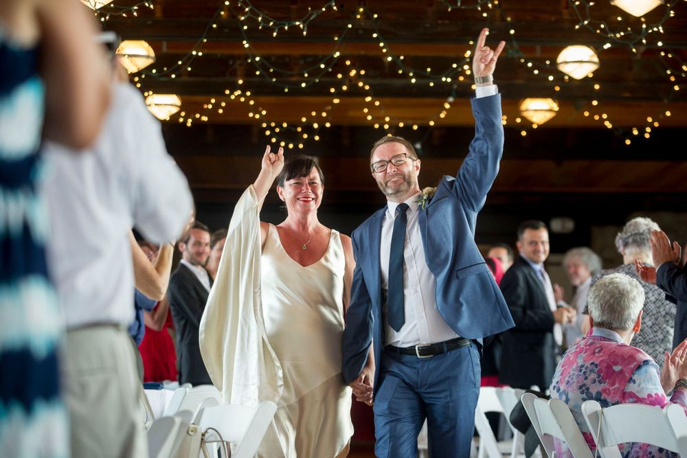 Joyful bride and groom raise their hands triumphantly as they enter their wedding reception hall.