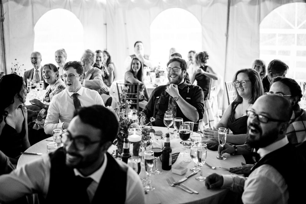 Wedding guests seated at long reception tables during speeches in black and white photo.
