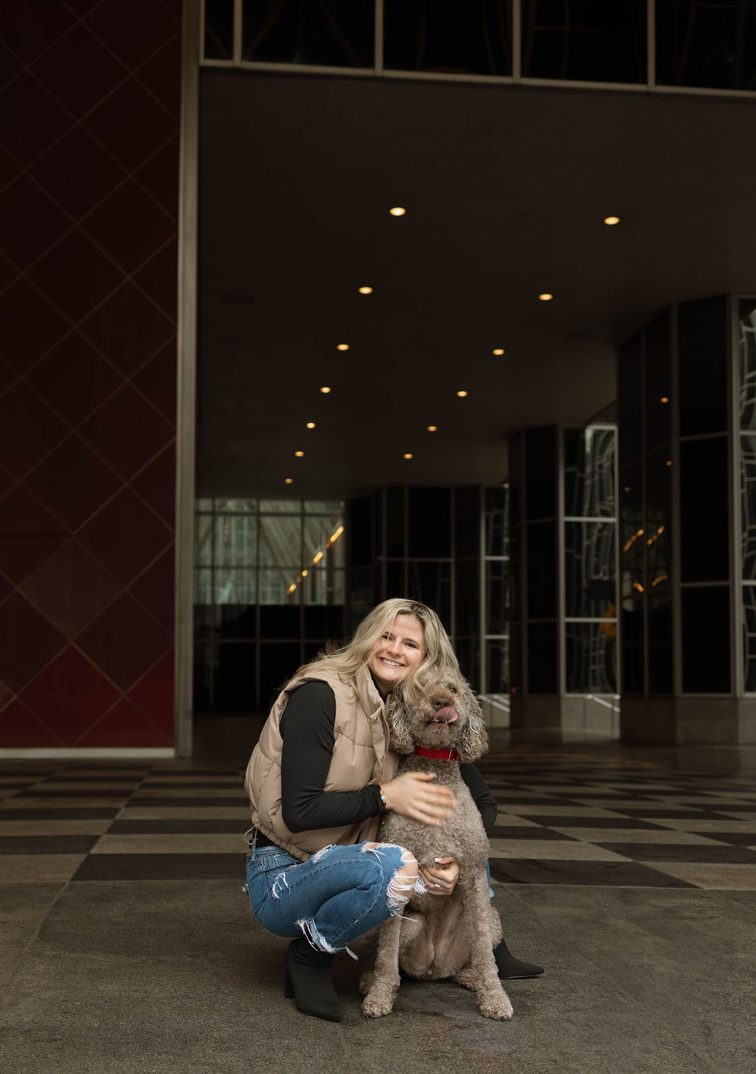 A playful dog jumps up to greet its owner in front of a large decorated Christmas tree in an urban setting.