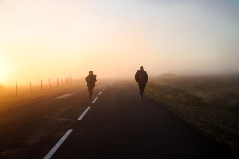 Deux silhouettes de coureurs sur une route droite, plongée dans un brouillard doré à la lumière du matin.