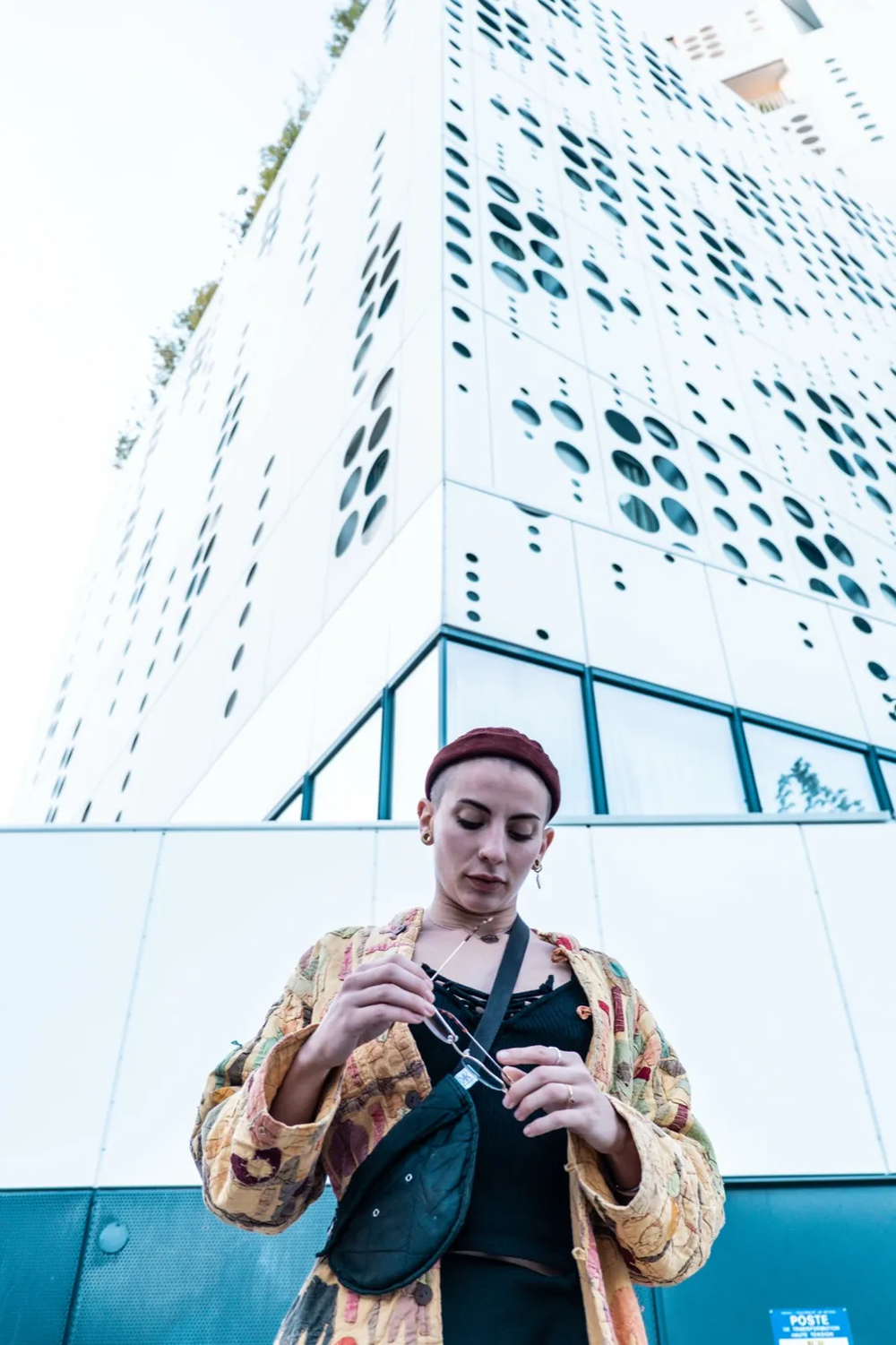 Portrait en contre-plongée d’un homme debout devant un immeuble moderne, lumière blanche.