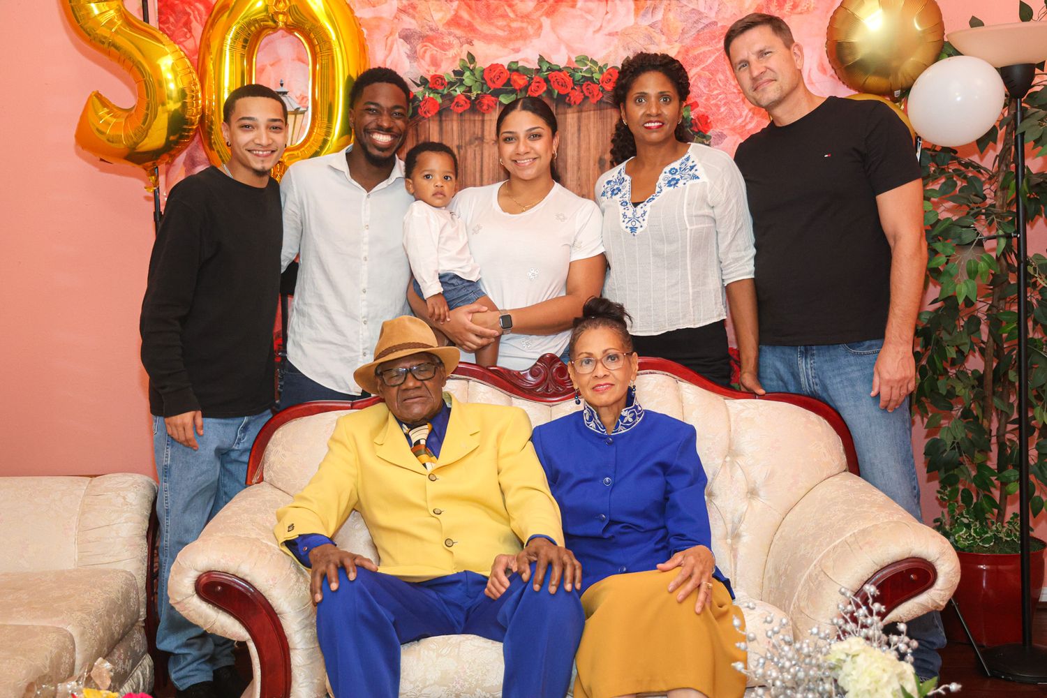 Family gathering for 50th celebration with gold balloons and pink floral background.