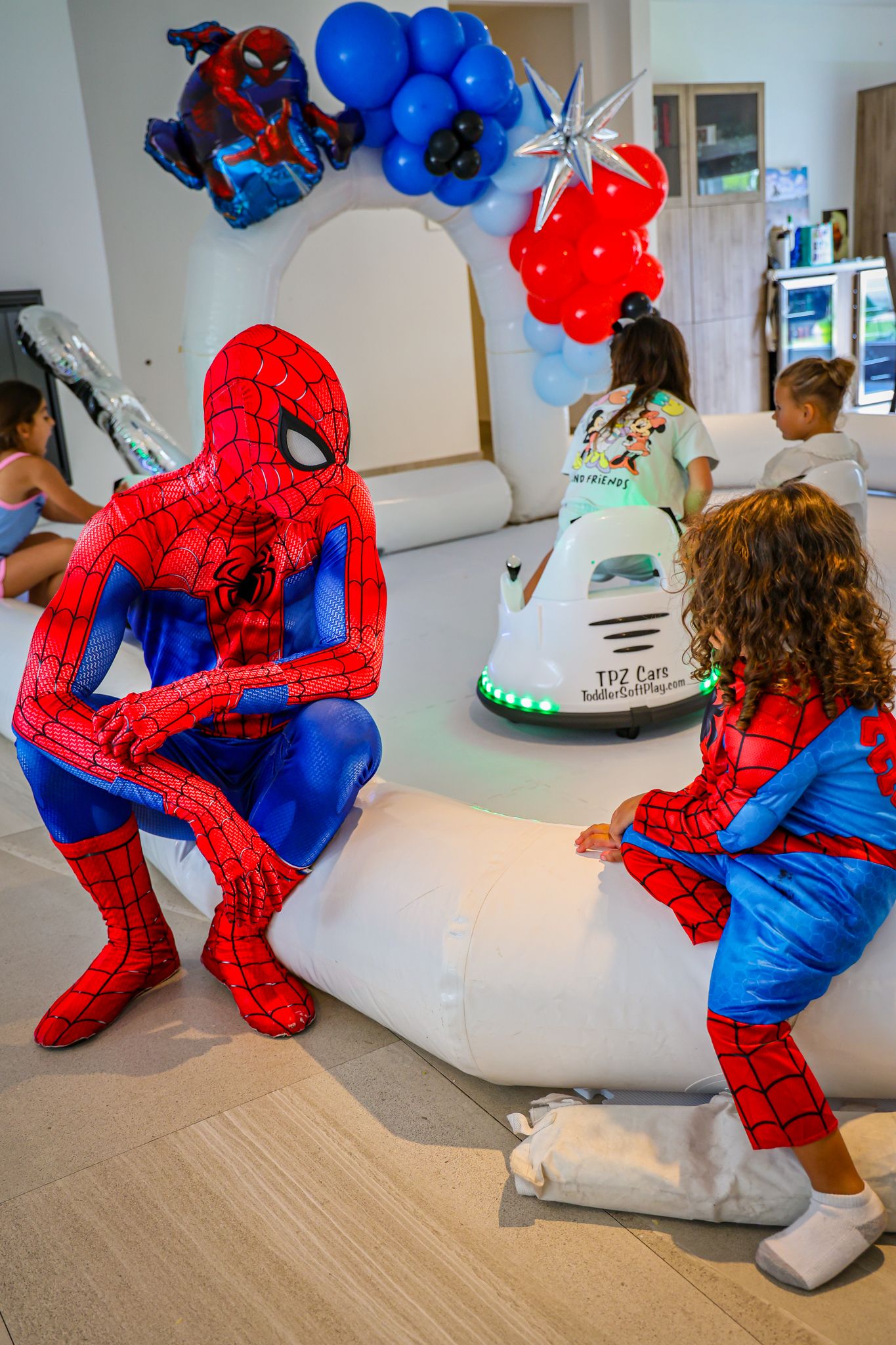 Spider-Man entertainer performing acrobatic moves at a party with blue balloons in the background.