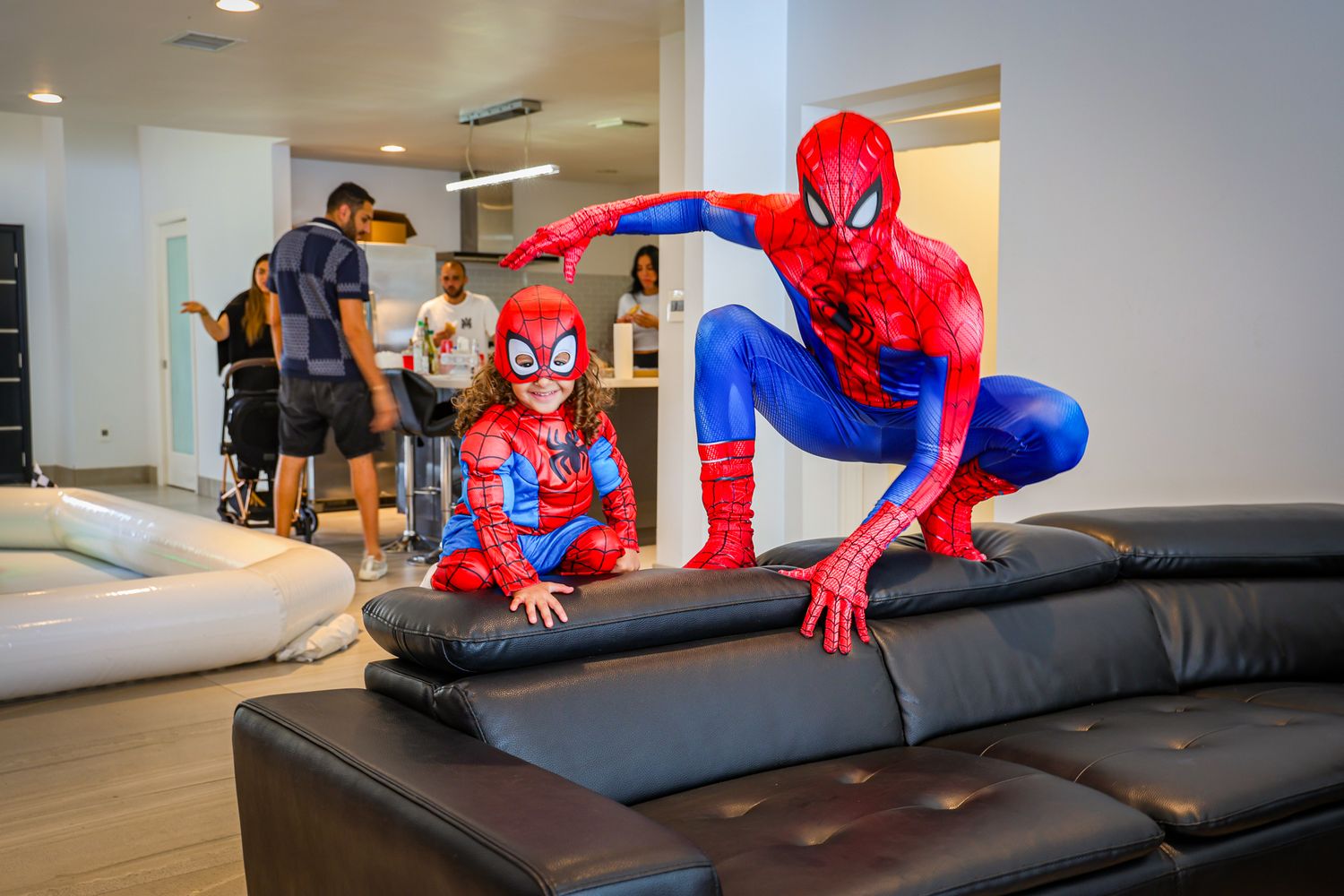Spider-Man costume performer doing stunts on a black leather couch at an indoor event.