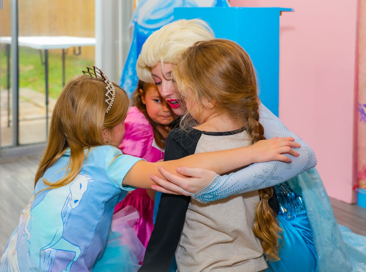 Children in blue and pink clothing embrace in a group hug at school.