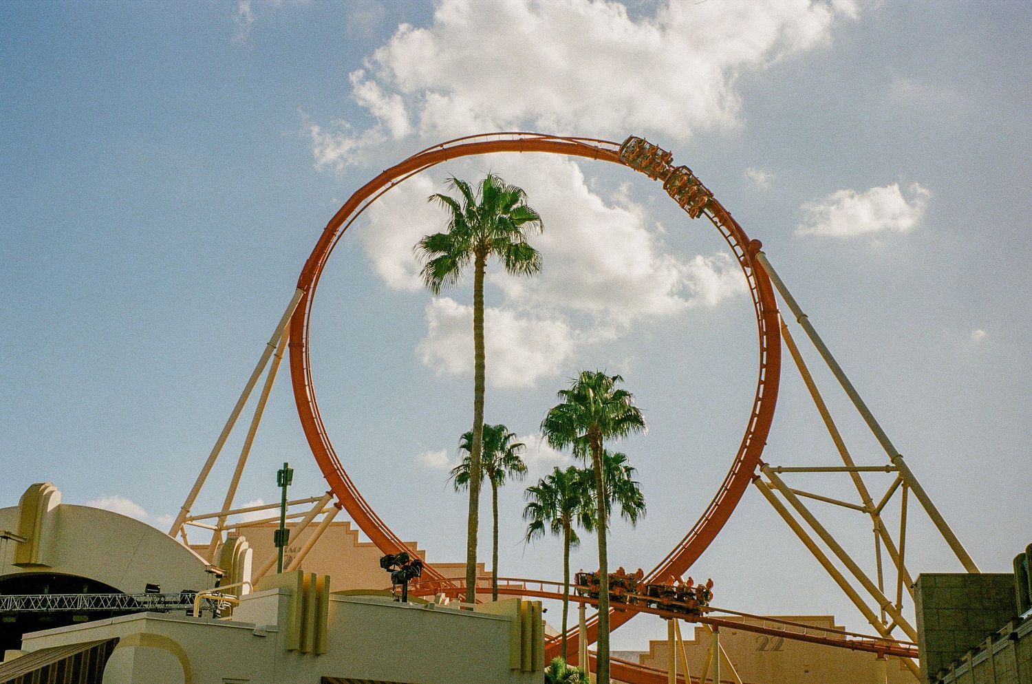 Large circular roller coaster loop with palm trees against blue sky.