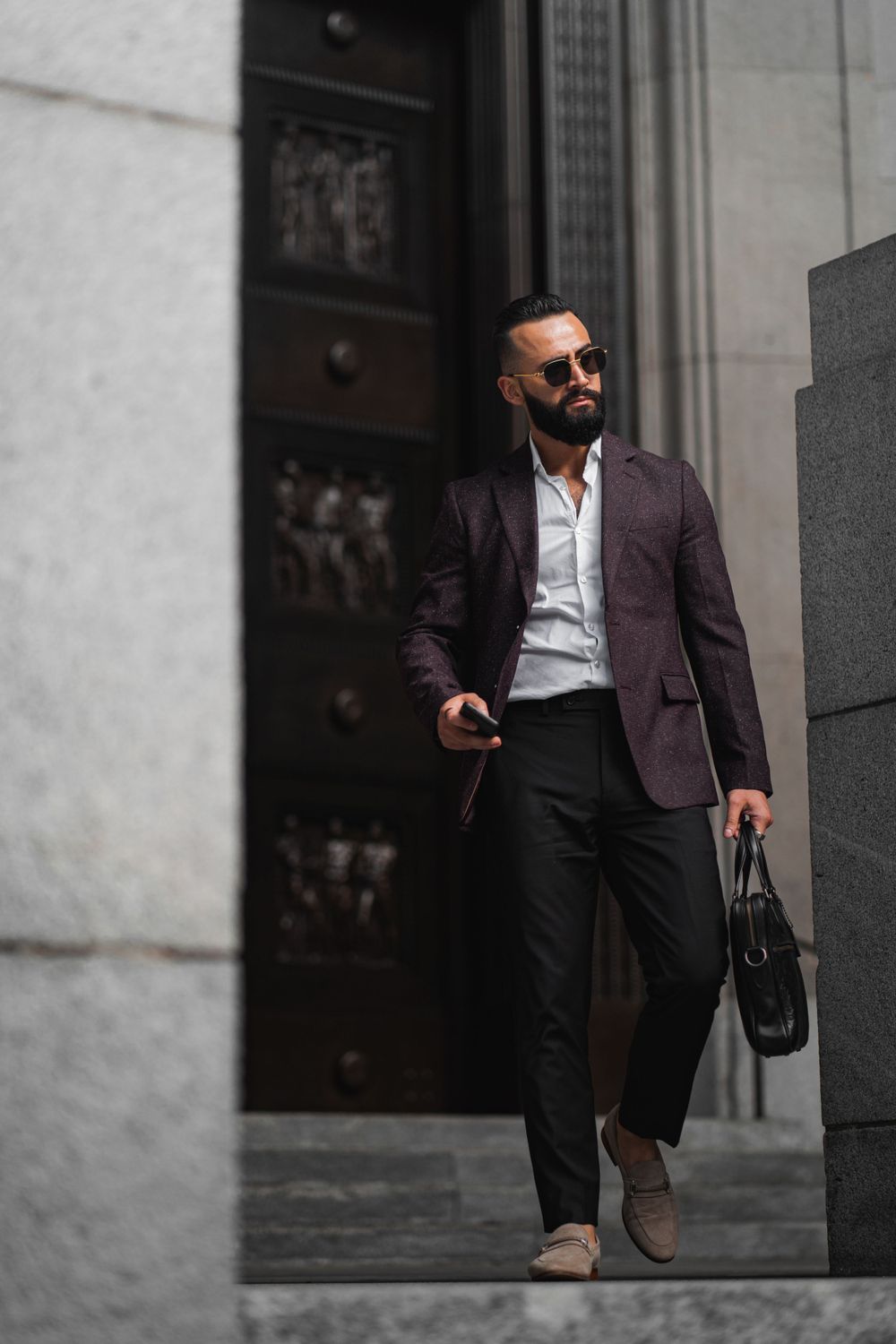 Professional man in blazer and sunglasses walking down urban steps with leather bag. Mtlshutter photography