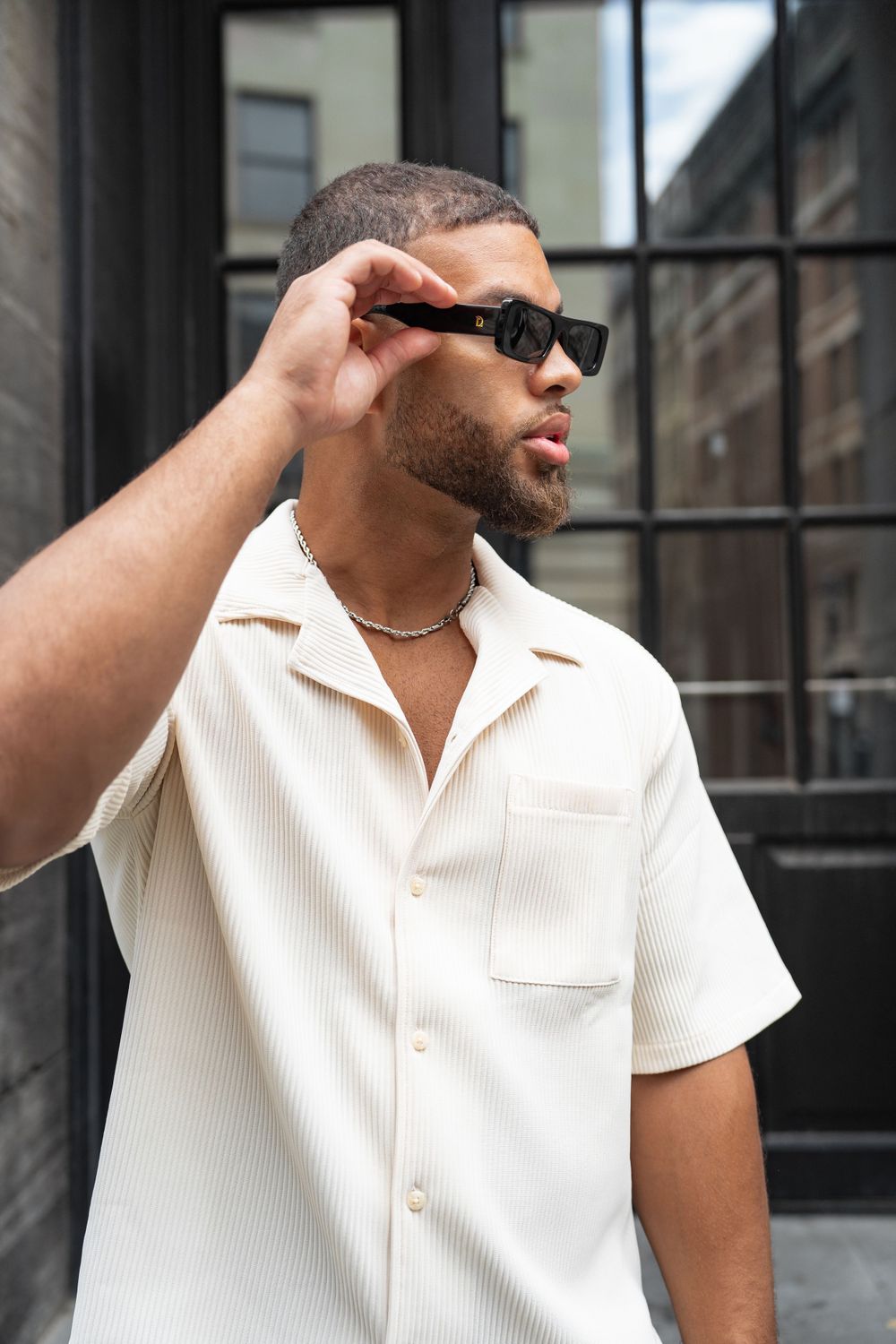 Person in white summer shirt adjusting sunglasses against urban backdrop. Mtlshutter photography