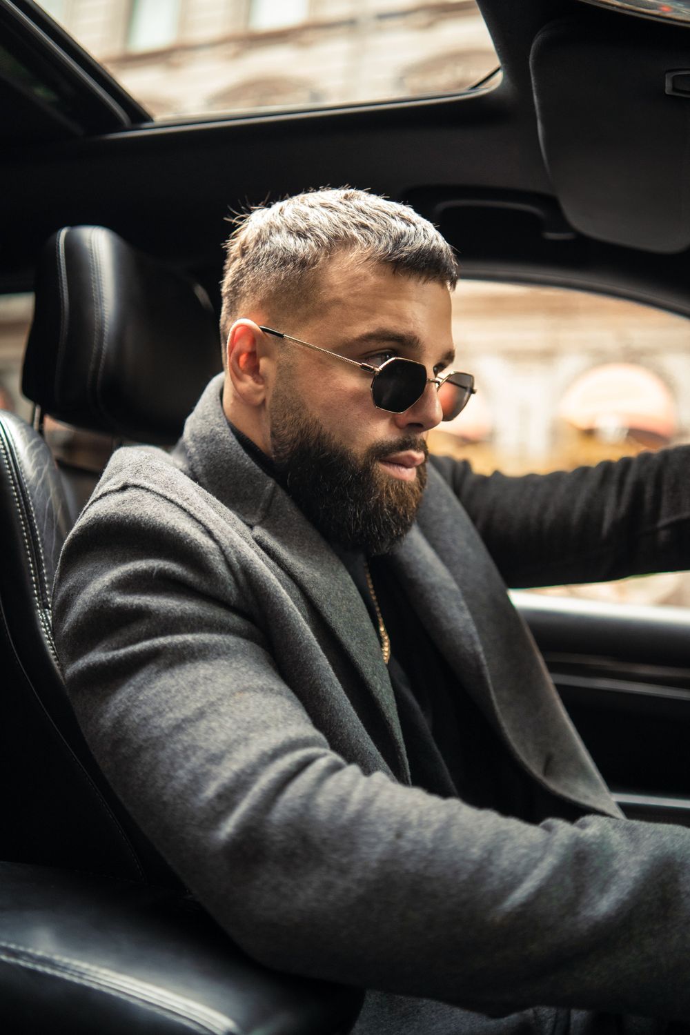 Person in grey coat and sunglasses sitting in driver's seat of luxury car. Mtlshutter photography