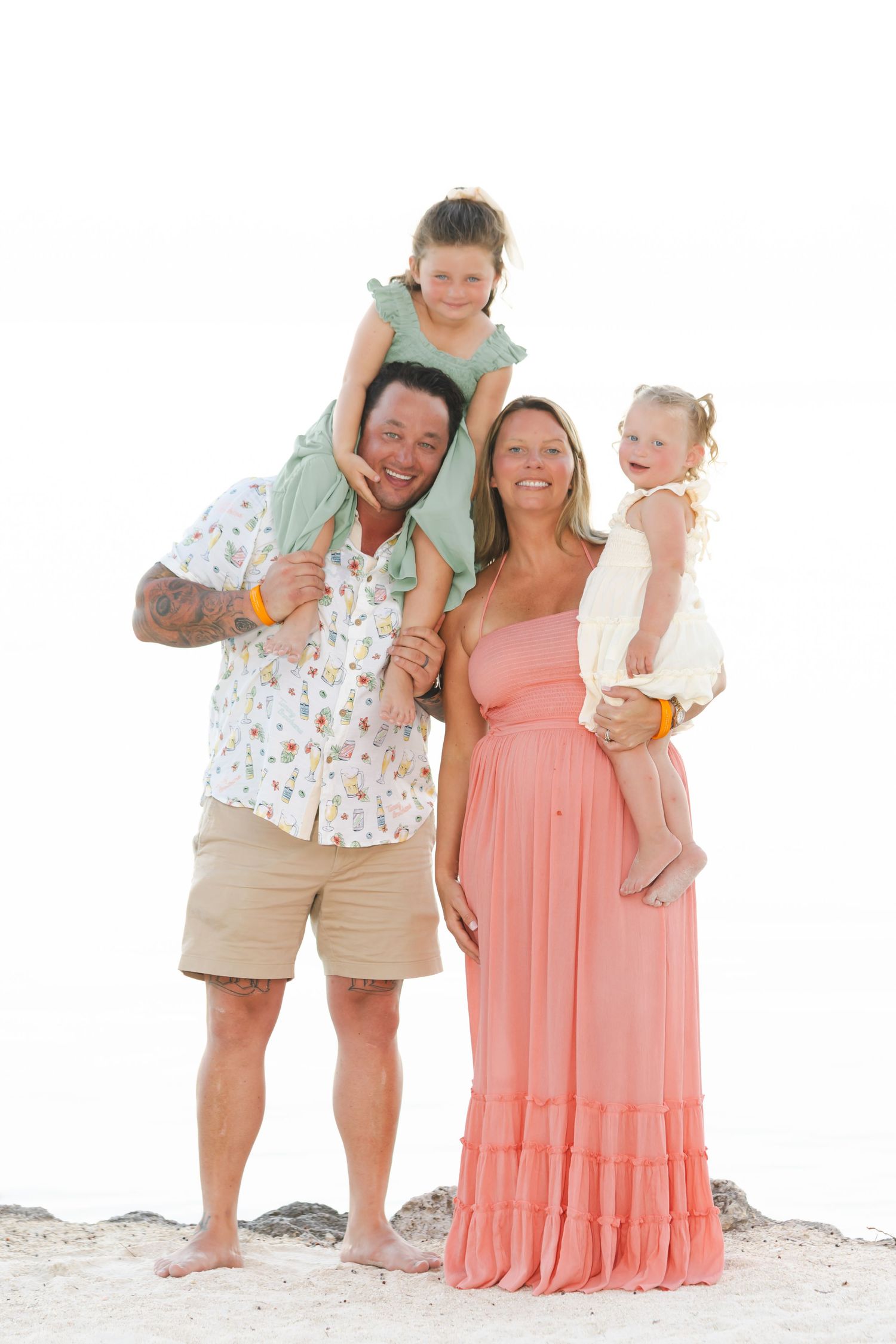 Beach family photoshoot with parents and children wearing coordinated coral and white outfits.