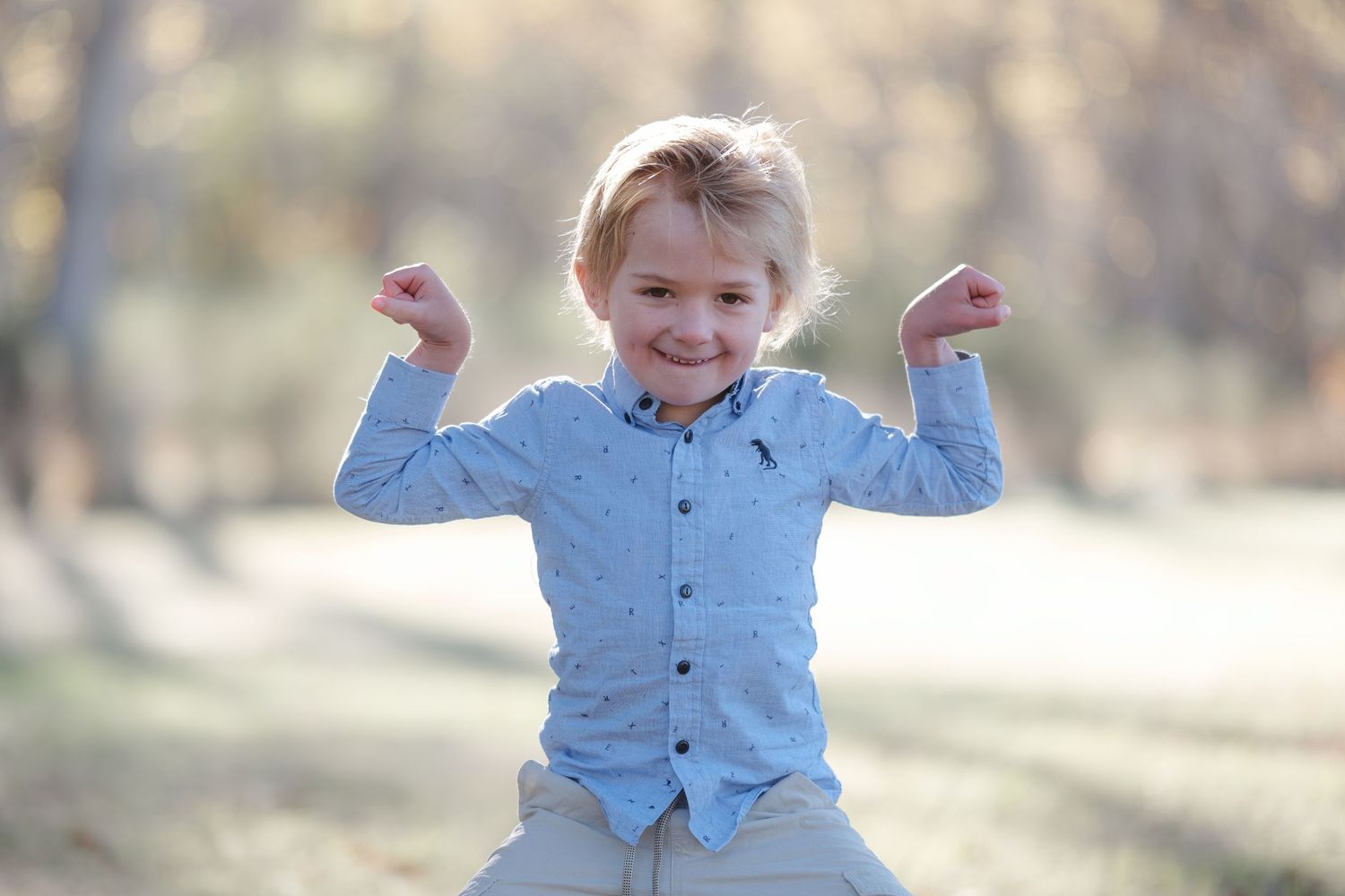 Young child in light blue shirt plays and poses outdoors in natural setting.