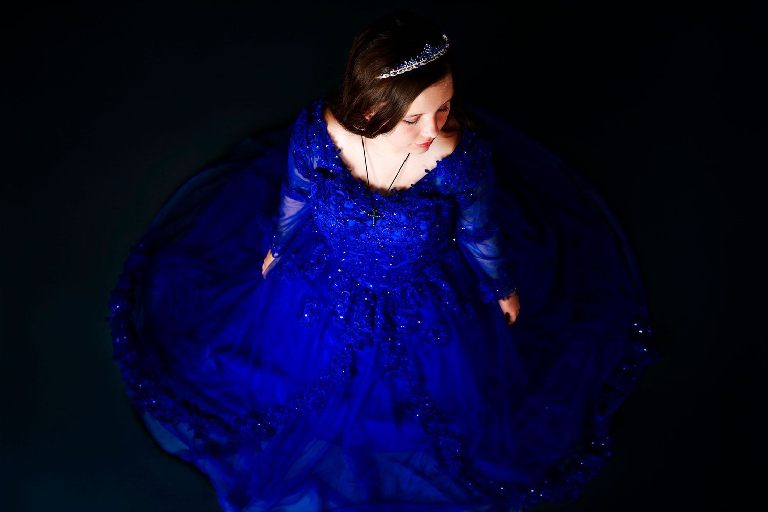 Looking down at a person wearing a flowing royal blue formal gown illuminated against a dark background.