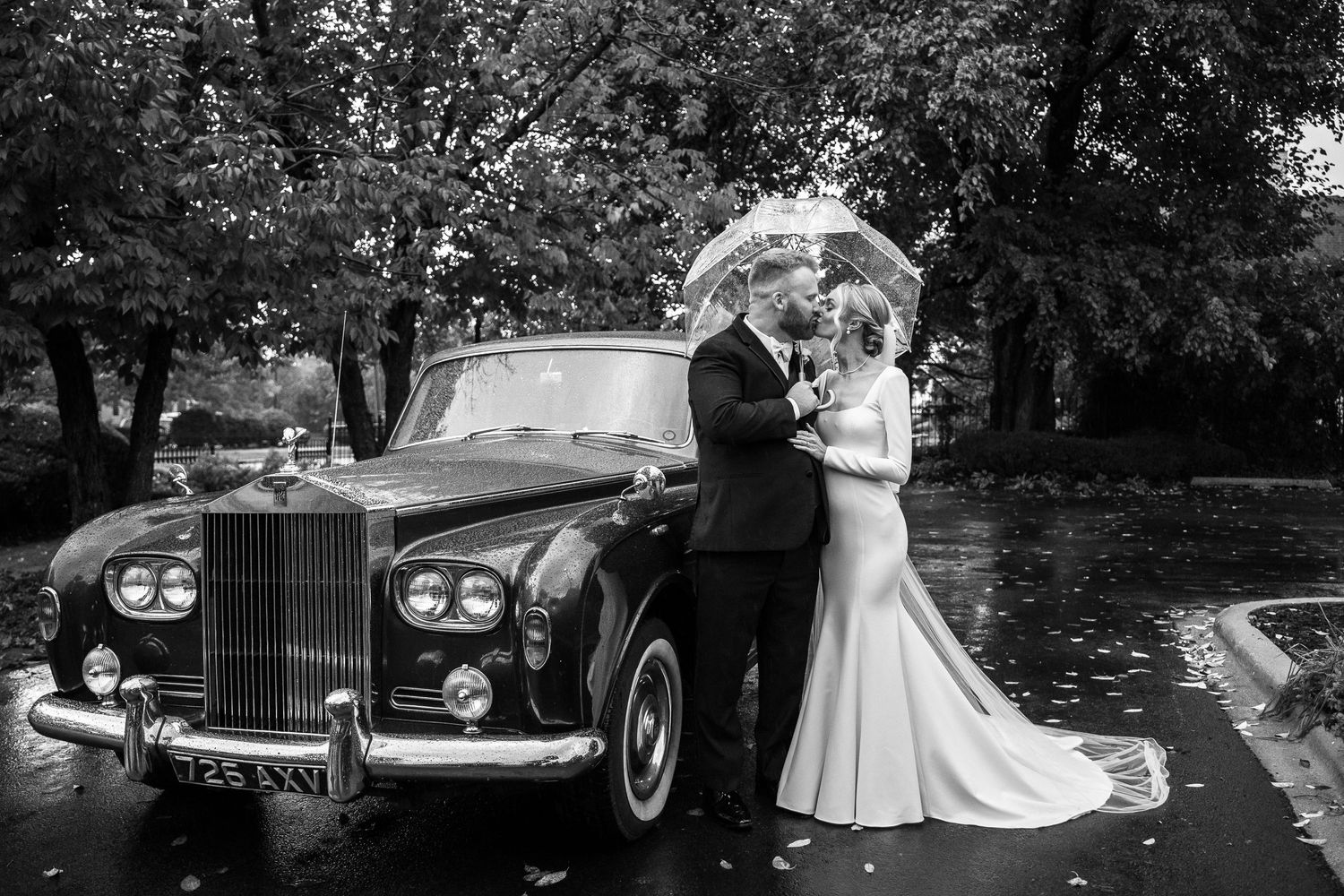 Elegant wedding couple posing with classic Rolls Royce in black and white photography.